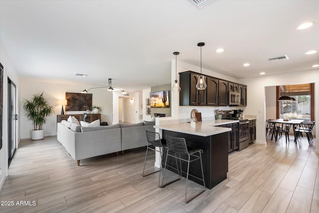 kitchen featuring kitchen peninsula, dark brown cabinets, pendant lighting, appliances with stainless steel finishes, and a breakfast bar area