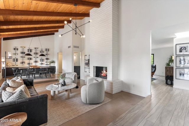 living room featuring wooden ceiling, high vaulted ceiling, a notable chandelier, a large fireplace, and beamed ceiling