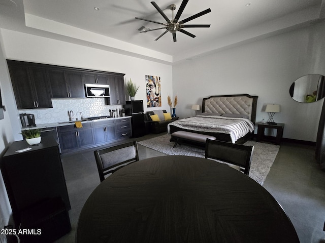 bedroom featuring ceiling fan, black refrigerator, sink, and a tray ceiling