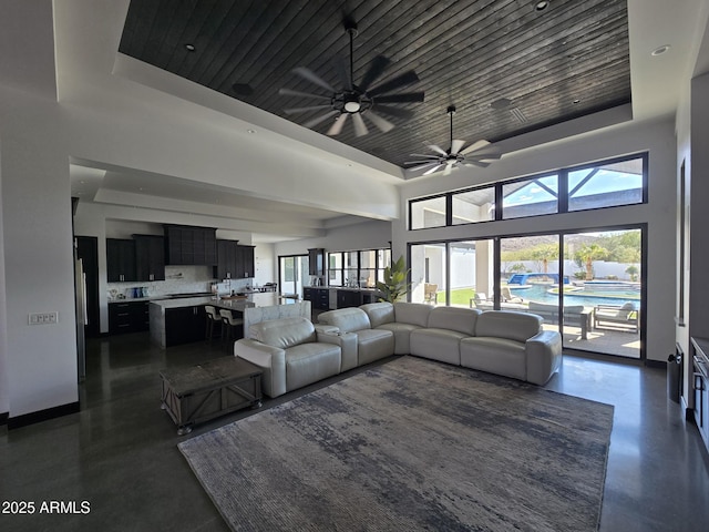 living room featuring a high ceiling, ceiling fan, and a tray ceiling