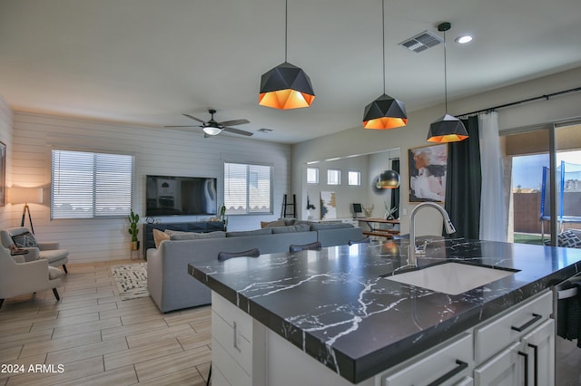 kitchen featuring pendant lighting, white cabinetry, sink, and an island with sink