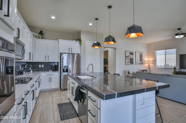 kitchen featuring appliances with stainless steel finishes, wood walls, white cabinetry, and a large island with sink