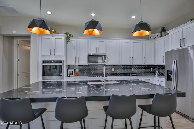 kitchen with hanging light fixtures, white cabinetry, a center island with sink, and stainless steel appliances