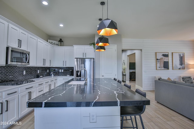 kitchen featuring pendant lighting, wood walls, a spacious island, sink, and stainless steel appliances