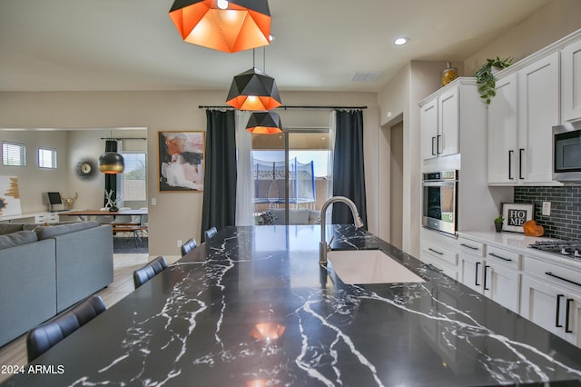 kitchen with decorative backsplash, stainless steel appliances, sink, white cabinets, and hanging light fixtures