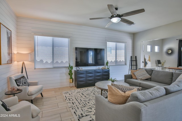 living room featuring ceiling fan, a healthy amount of sunlight, light hardwood / wood-style floors, and wooden walls