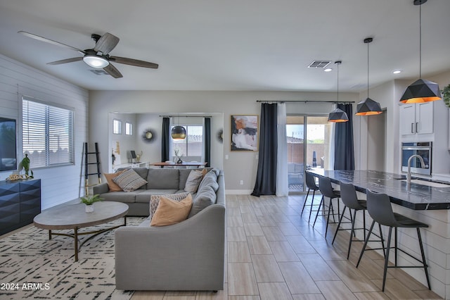 living room featuring light hardwood / wood-style flooring, ceiling fan, wood walls, and sink