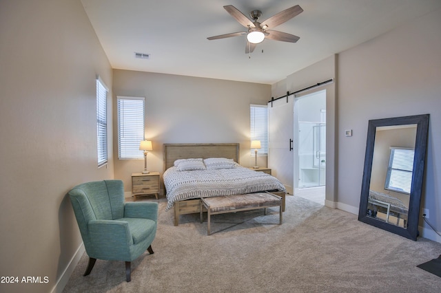 bedroom featuring connected bathroom, a barn door, ceiling fan, and carpet