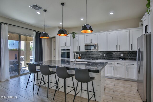 kitchen featuring a kitchen island with sink, white cabinets, and stainless steel appliances