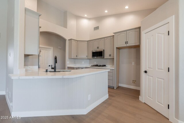 1062 N Robin Ln, Mesa, AZ 85213 - kitchen with stainless steel microwave, a peninsula, a sink, light wood-type flooring, and gas stovetop