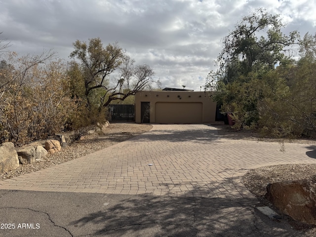 adobe home featuring a garage, fence, decorative driveway, and stucco siding