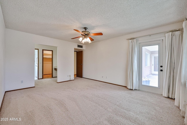 empty room with visible vents, a ceiling fan, a textured ceiling, baseboards, and light colored carpet