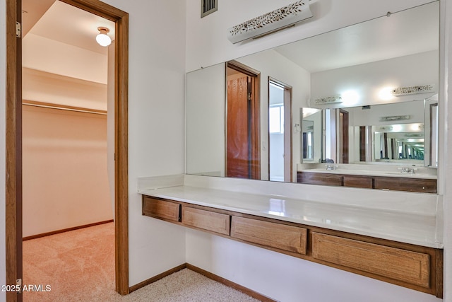 bathroom with visible vents, vanity, a walk in closet, and baseboards