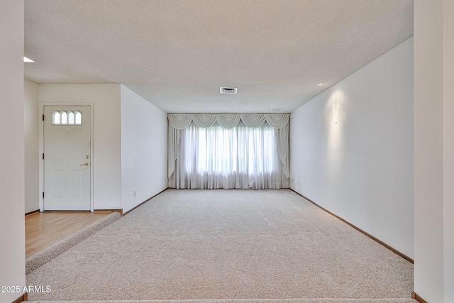 carpeted spare room with baseboards, visible vents, and a textured ceiling