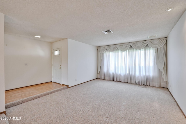 carpeted empty room with baseboards, visible vents, and a textured ceiling