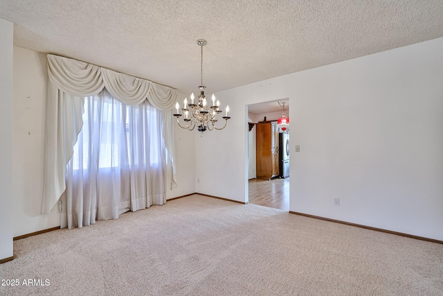 carpeted spare room featuring baseboards, a textured ceiling, and a chandelier