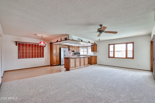 kitchen featuring brown cabinets, appliances with stainless steel finishes, open floor plan, and a healthy amount of sunlight