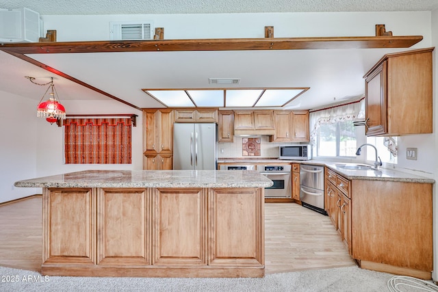 kitchen with visible vents, a kitchen island, light wood-style flooring, a sink, and stainless steel appliances