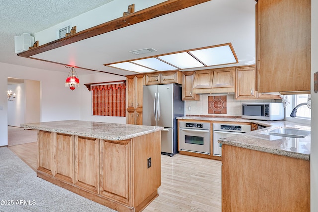 kitchen with a center island, light stone counters, appliances with stainless steel finishes, custom exhaust hood, and a sink