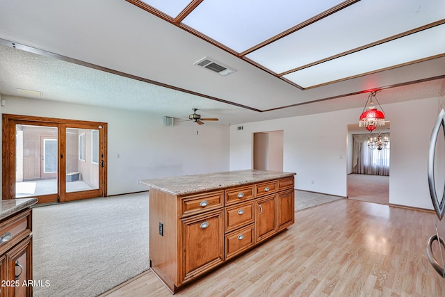 kitchen featuring brown cabinetry, visible vents, light wood finished floors, light countertops, and a textured ceiling