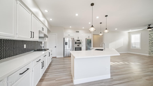 kitchen featuring appliances with stainless steel finishes, backsplash, sink, a center island with sink, and white cabinets