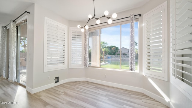 unfurnished dining area with a notable chandelier and light wood-type flooring