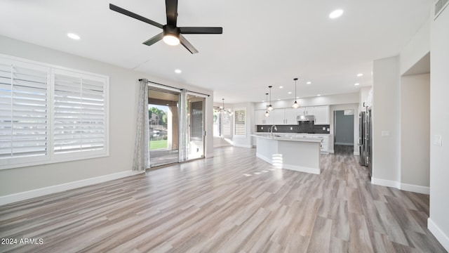 unfurnished living room with sink, ceiling fan with notable chandelier, and light hardwood / wood-style flooring