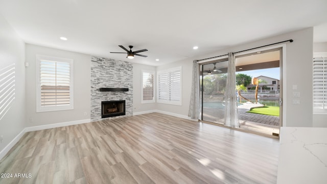 unfurnished living room with ceiling fan, a stone fireplace, and light wood-type flooring