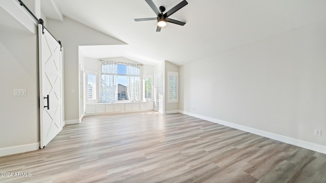 interior space with vaulted ceiling, ceiling fan, a barn door, and light hardwood / wood-style floors