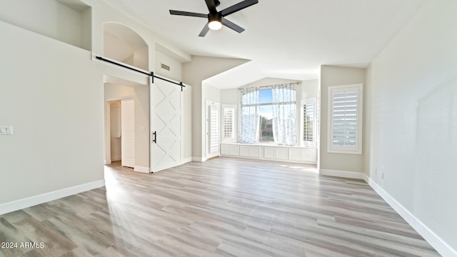 spare room with a barn door, light hardwood / wood-style flooring, ceiling fan, and lofted ceiling