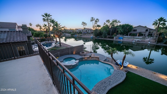 pool at dusk with a water view, an in ground hot tub, and a patio