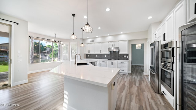 kitchen with sink, hanging light fixtures, light stone counters, backsplash, and white cabinets