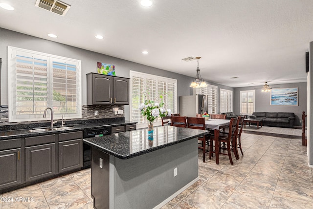 kitchen with dishwasher, ceiling fan with notable chandelier, sink, stainless steel fridge, and a kitchen island