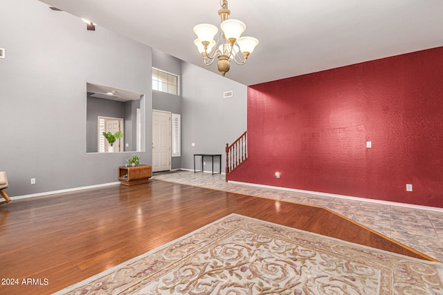 unfurnished room featuring an inviting chandelier, wood-type flooring, and a towering ceiling