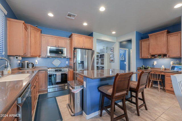 kitchen with light tile patterned floors, appliances with stainless steel finishes, a kitchen island, and a sink