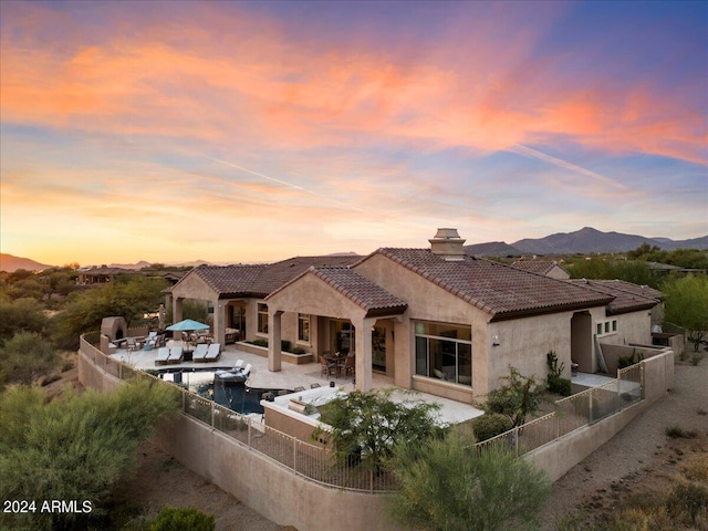 back house at dusk with a fenced in pool, a mountain view, and a patio area