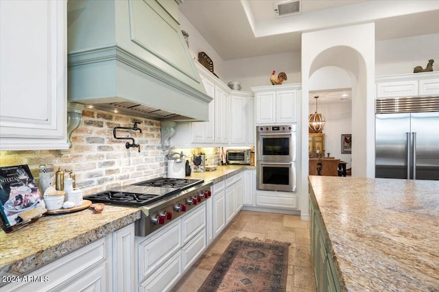 kitchen with white cabinets, premium range hood, appliances with stainless steel finishes, and tasteful backsplash