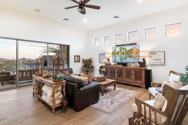 living room with light hardwood / wood-style flooring, a towering ceiling, and ceiling fan