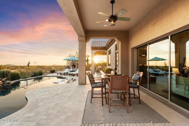 patio terrace at dusk with a fenced in pool and ceiling fan