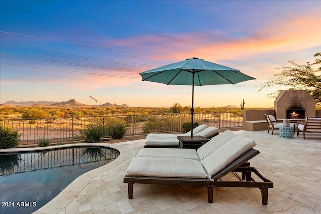 patio terrace at dusk featuring a fenced in pool, an outdoor fireplace, and a mountain view