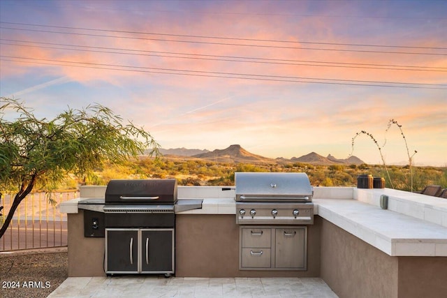 patio terrace at dusk with exterior kitchen, a mountain view, and a grill