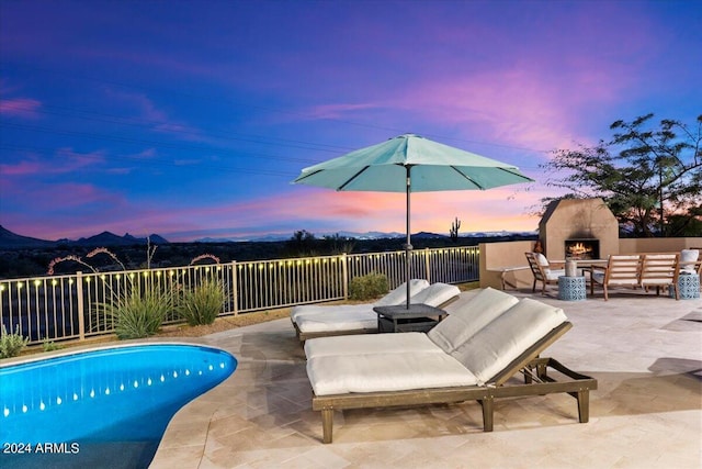 patio terrace at dusk with a fenced in pool and an outdoor living space with a fireplace