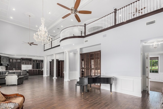 living room featuring crown molding, a towering ceiling, dark wood-type flooring, and ceiling fan with notable chandelier