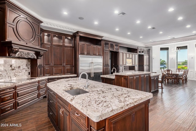 kitchen with stainless steel built in fridge, sink, an island with sink, dark brown cabinets, and dark hardwood / wood-style flooring