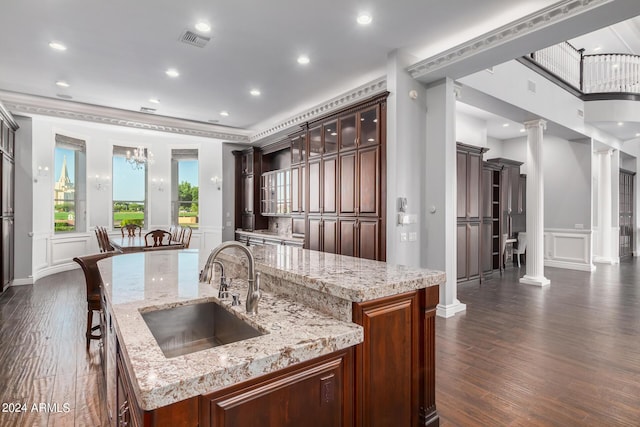 kitchen with light stone countertops, sink, dark hardwood / wood-style flooring, decorative columns, and an island with sink