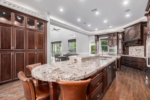 kitchen with a large island, ceiling fan, sink, a kitchen breakfast bar, and dark hardwood / wood-style flooring