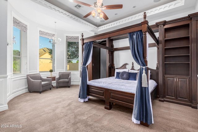 carpeted bedroom featuring ceiling fan with notable chandelier, crown molding, and a tray ceiling