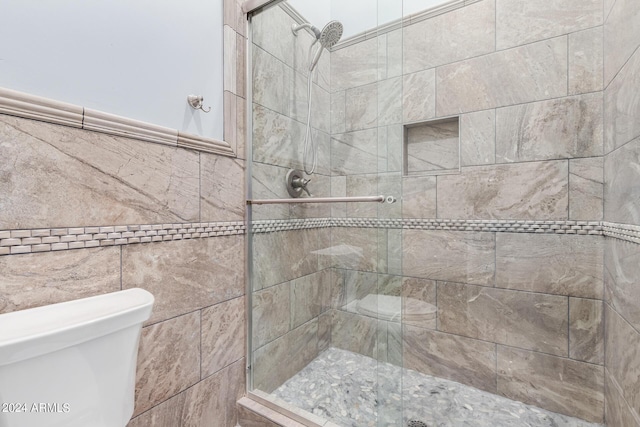 bathroom with toilet, a shower with shower door, and tile walls