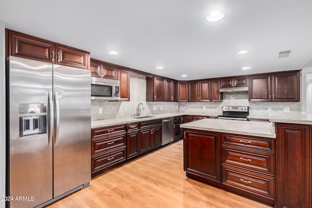 kitchen with appliances with stainless steel finishes, backsplash, light stone counters, sink, and light hardwood / wood-style flooring