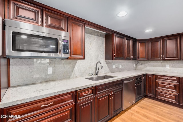 kitchen with sink, light hardwood / wood-style flooring, light stone countertops, appliances with stainless steel finishes, and tasteful backsplash